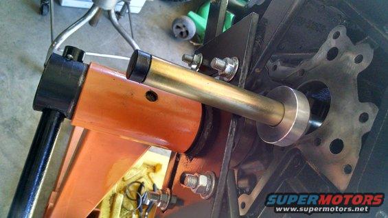 Engine block with a brass tool inserted into a circular opening, attached to an orange support