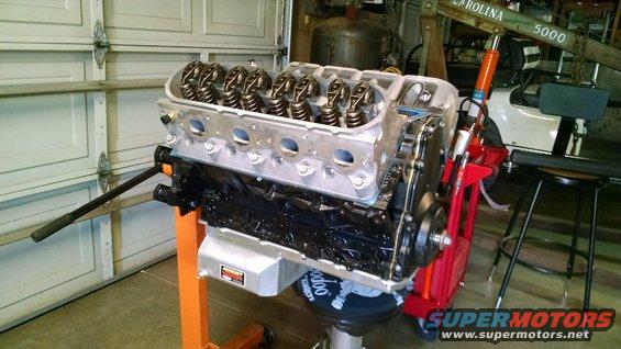 Engine on an orange stand with a black oil pan and silver accents, in a garage