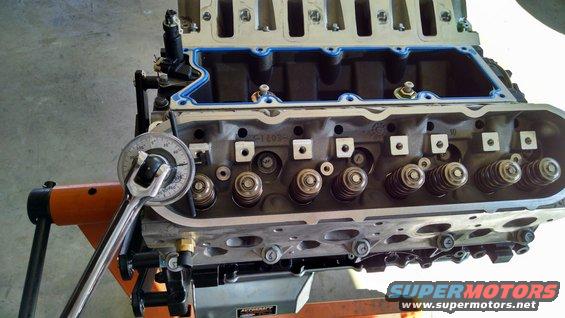 Engine cylinder head on an orange stand with a torque wrench measuring valve spring pressure