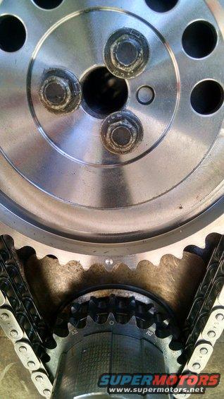Close-up of engine timing chain and sprockets with visible bolts and SuperMotors.net logo
