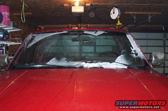Red pickup truck hood and windshield covered in snow, parked in a garage