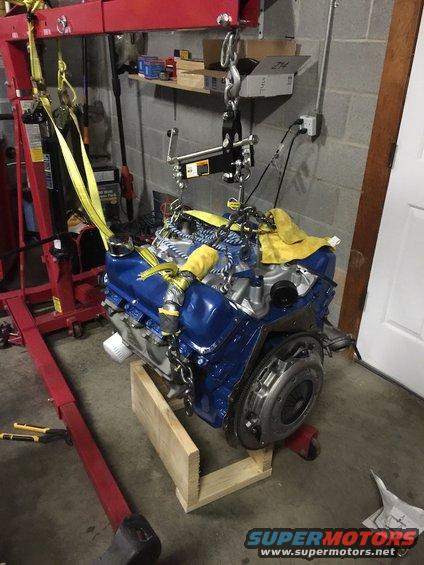 Blue engine with clutch assembly, suspended by engine hoist and straps