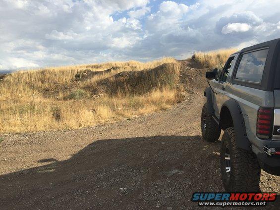 Gray Ford Bronco with off-road tires on a dirt trail, dry grass hills in background