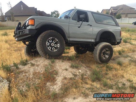 Gray 1988 Ford Bronco with aftermarket bumper and large tires on a dirt mound