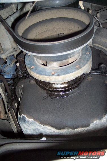 Close-up of a dusty engine pulley and a greasy oil pan with a leaking gasket