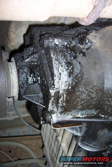 Differential housing covered in heavy grease and grime, with a driveshaft flange visible on the left
