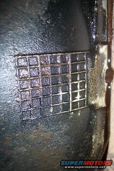 Close-up of a greasy metal part with a grid pattern embossed on it