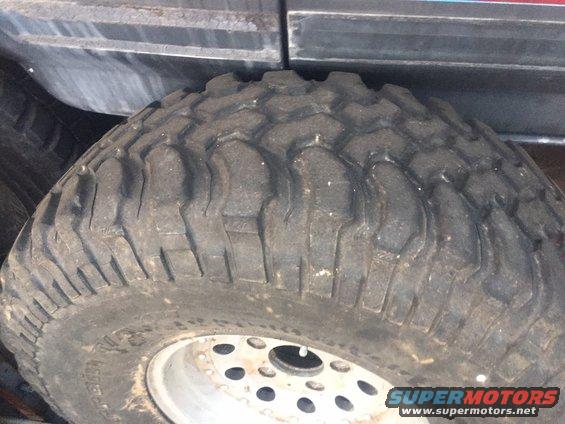 Close-up of a large off-road tire with aggressive tread pattern and a silver wheel with multiple lug holes