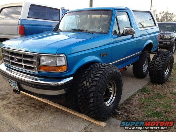 Blue Ford Bronco with large off-road tires, lifted suspension, and a white roof