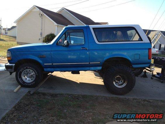 Blue 1995 Ford Bronco with lifted suspension and large tires, parked on a driveway
