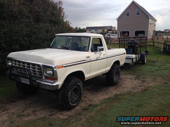 White 1979 Ford Bronco with a bull bar and trailer, parked on a dirt path