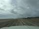 1979 Ford Bronco - A wide expanse of beach with tire tracks leading towards the ocean under a cloudy sky.
