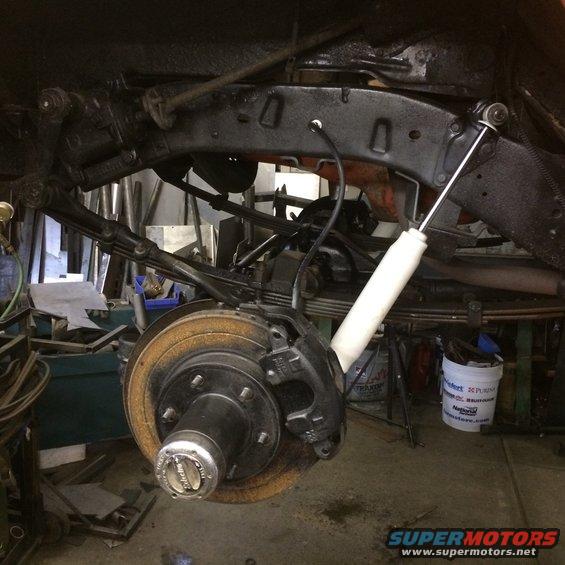 Close-up of a vehicle's rear suspension with leaf springs, shock absorber, and brake rotor