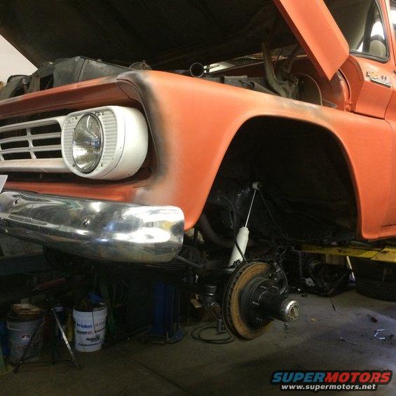 Orange pickup truck front end, hood open, showing suspension work. Grille indicates 1960s era
