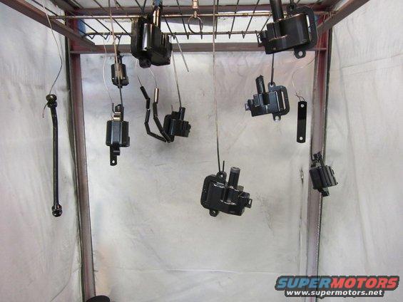 Black ignition coils and parts hanging to dry in a spray booth