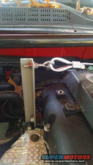 Engine bay with metal bracket, cable, and black cover. Watermark 'SUPERMOTORS.NET'