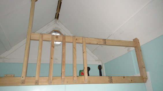 Wooden beams forming a loft structure with a small octagonal window in the background
