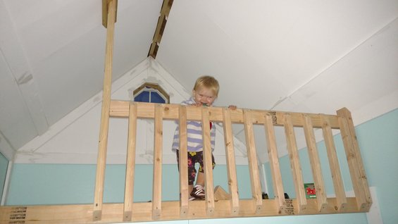 Child standing behind a wooden railing in a playhouse loft