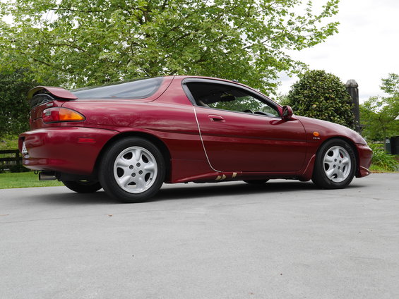 Red 1993 Mazda MX-3 coupe parked on concrete, side view