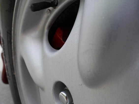 Close-up of a silver alloy wheel with a red brake caliper visible through an opening