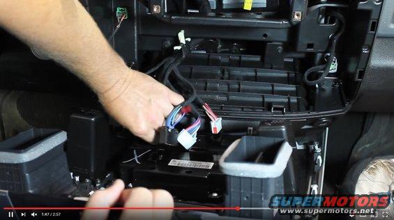 Hands working on car dashboard wiring harness with various connectors