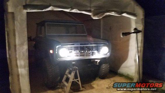 Dark blue Ford Bronco with chrome grille and headlights on, parked inside a tent