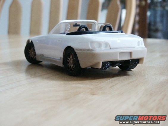 White toy convertible with black interior and gold-spoked wheels, viewed from the rear