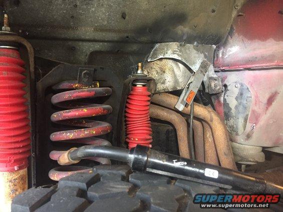Close-up of red coil springs, red shock absorbers, and rusty exhaust pipes under a vehicle