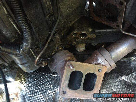 Engine exhaust manifold with two ports, connected to piping. Some wiring and engine block visible