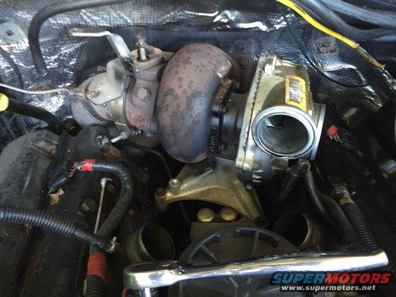 Turbocharger and exhaust manifold assembly with hoses and wiring. A wrench is visible in the foreground