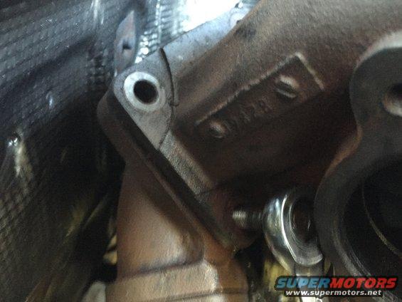 Close-up of turbocharger exhaust housing with a wrench on a bolt. Numbers are visible on the housing