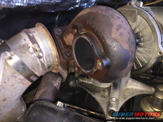 Rusty turbocharger housing with exhaust pipe connected. Supermotors.net logo visible