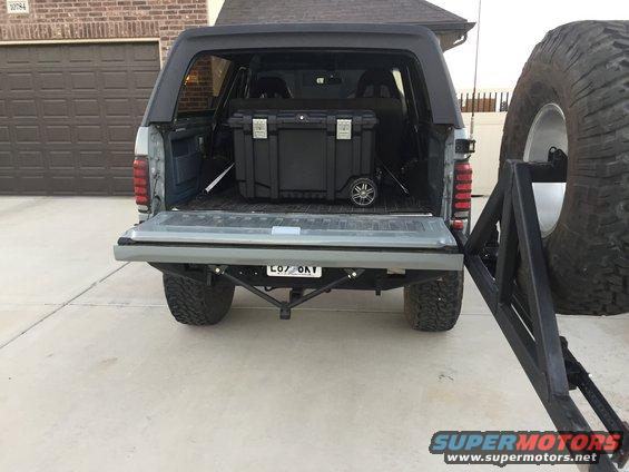 Gray Ford Bronco with tailgate down, black storage box inside, and spare tire carrier on the right
