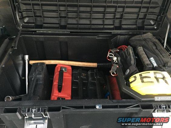 Open storage box in vehicle with axe, red toolbox, gloves, and yellow strap