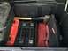 1988 Ford Bronco - A storage box contains various tools, including an axe and multiple tool cases, suggesting it is part of a vehicle's utility storage.