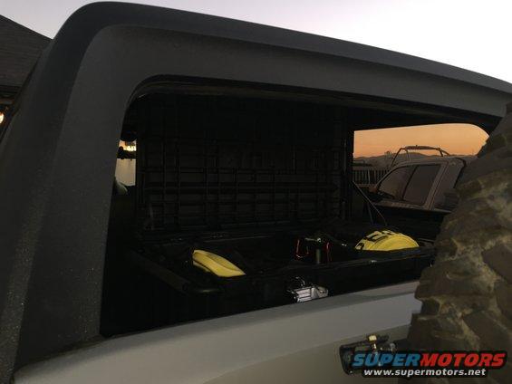 Open storage box with yellow items inside, viewed from rear of vehicle. Another vehicle is visible in the background