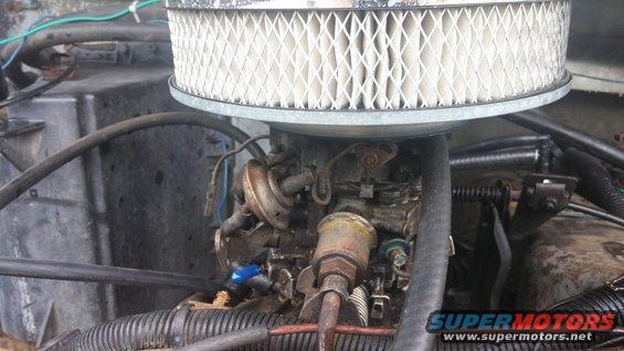 Engine carburetor with air filter above. Wires and hoses are visible