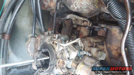 Engine carburetor with visible springs and metal components, some rust and oil stains