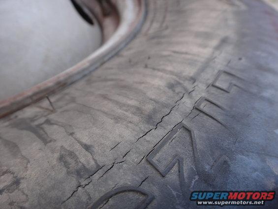 Close-up of a cracked tire sidewall with visible dry rot. Text is partially visible