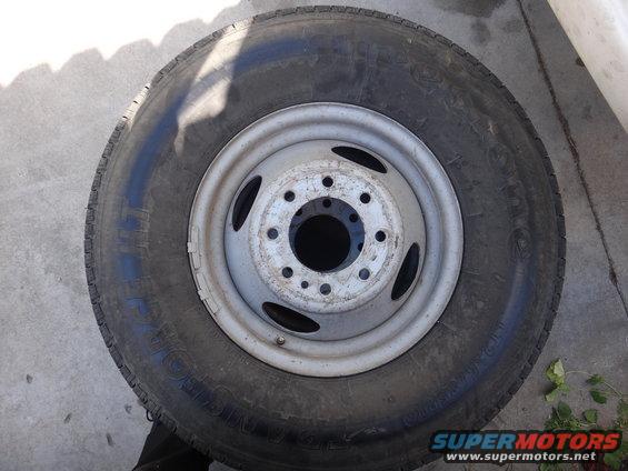 Wheel and tire assembly on concrete, showing a silver rim with multiple bolt holes and a black tire with visible tread
