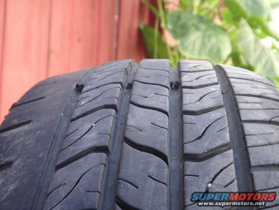 Close-up of a tire's tread pattern. There are small objects embedded in the rubber