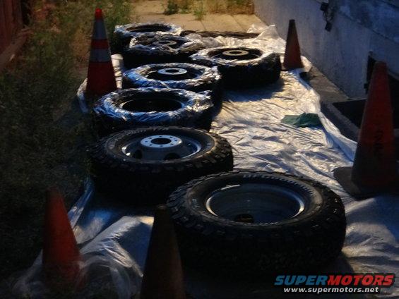 Several tires and wheels laid out on plastic sheeting with orange traffic cones