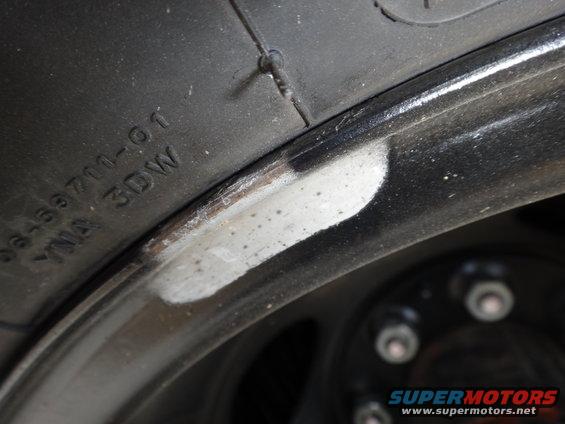 Close-up of a tire with markings and a black wheel rim showing some scuffs