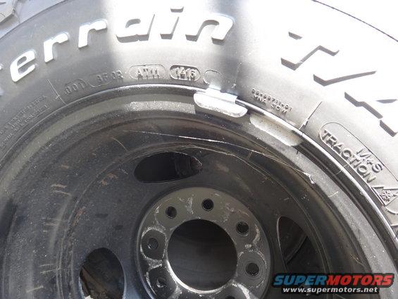 Close-up of a BFGoodrich All-Terrain tire on a black steel wheel with a wheel weight attached. Tire has '0416' marking