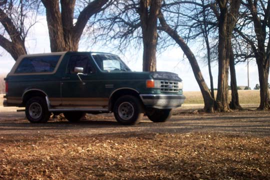Green 1987 Ford Bronco parked under trees
