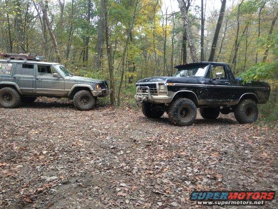 Black 1978 Ford Bronco with a brush guard and roof visor, parked on a dirt path in a forest