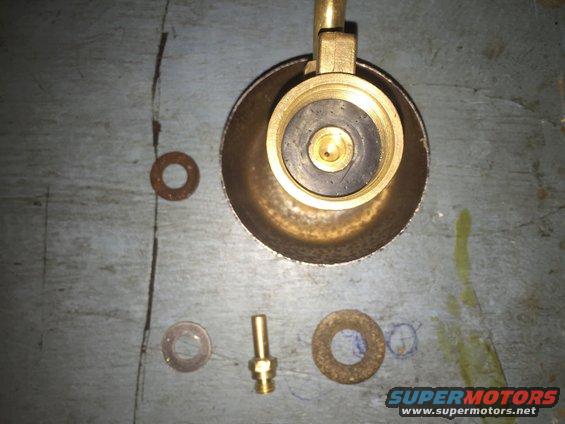 Brass valve fitting with rubber seal, next to three washers on a grey surface