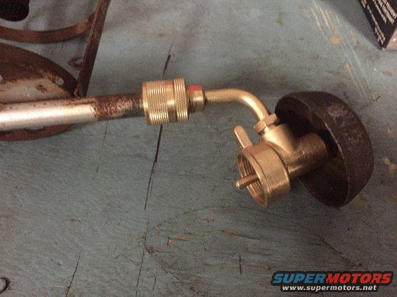 Brass torch fitting with a ribbed connector and a black cap, attached to a rusty metal tube