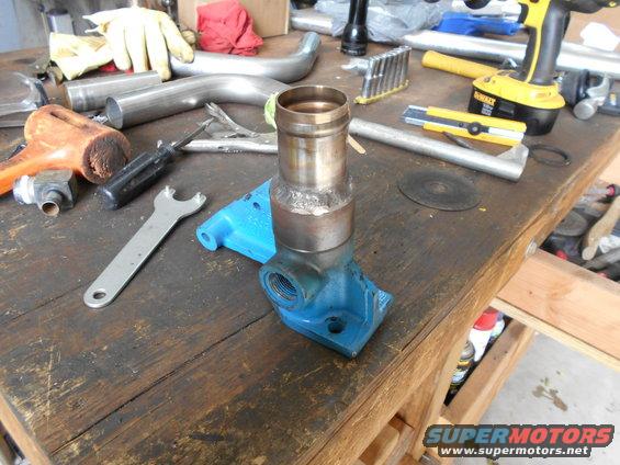 Workbench with various tools including a wrench, screwdriver, hammer, and a cordless drill, along with metal pipes and a blue bracket with a metal fitting