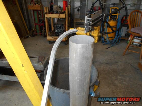 Metal pipe and curved metal strip near a rolling machine and air compressor in a workshop